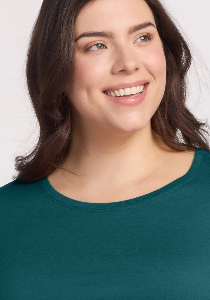 A woman with wavy brown hair smiles and looks to the side, wearing the Woolx Jenny 3/4 Sleeve Crew Neck shirt in Riverbank Green against a light background.