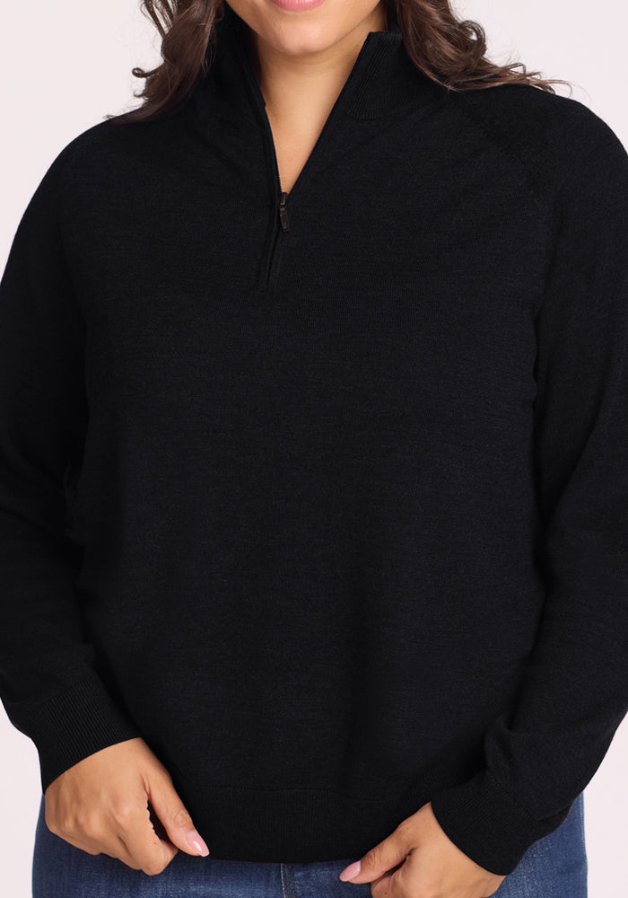 A person wears the Woolx Collins Half-Zip Sweater in black with blue jeans; their head is partially out of frame.
