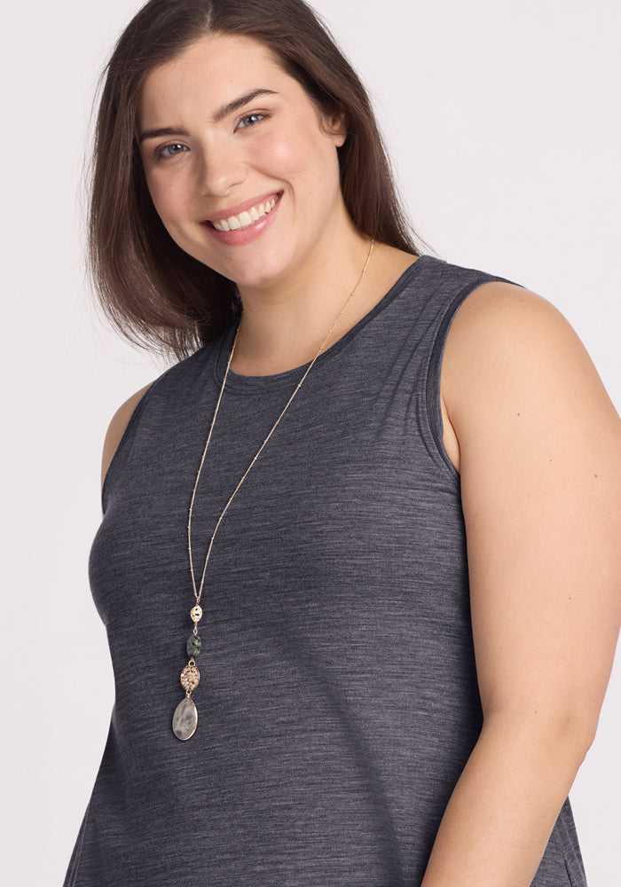 A woman with long brown hair smiles, wearing the Woolx Clara Dress in Cinder Melange and a long pendant necklace, set against a plain light background.