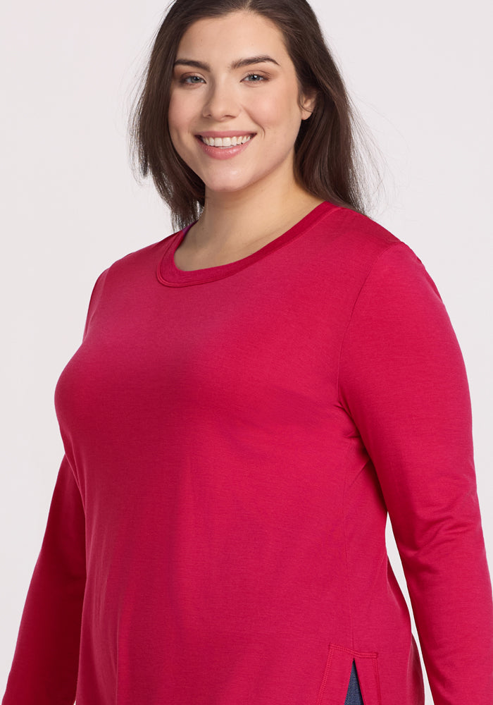 A woman with long brown hair wears the Woolx Hazel Tunic in Poppy Spark and smiles while standing against a plain light background.