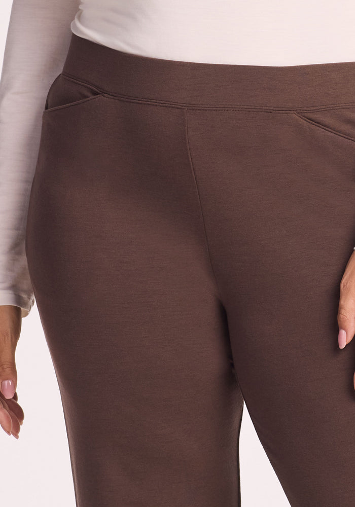 A person wearing Woolx Ellie Wide Leg Pants in Bracken and a white long-sleeve shirt stands with one hand by their side, the image focusing on the waist and upper legs to highlight the cozy Merino wool thermal style.
