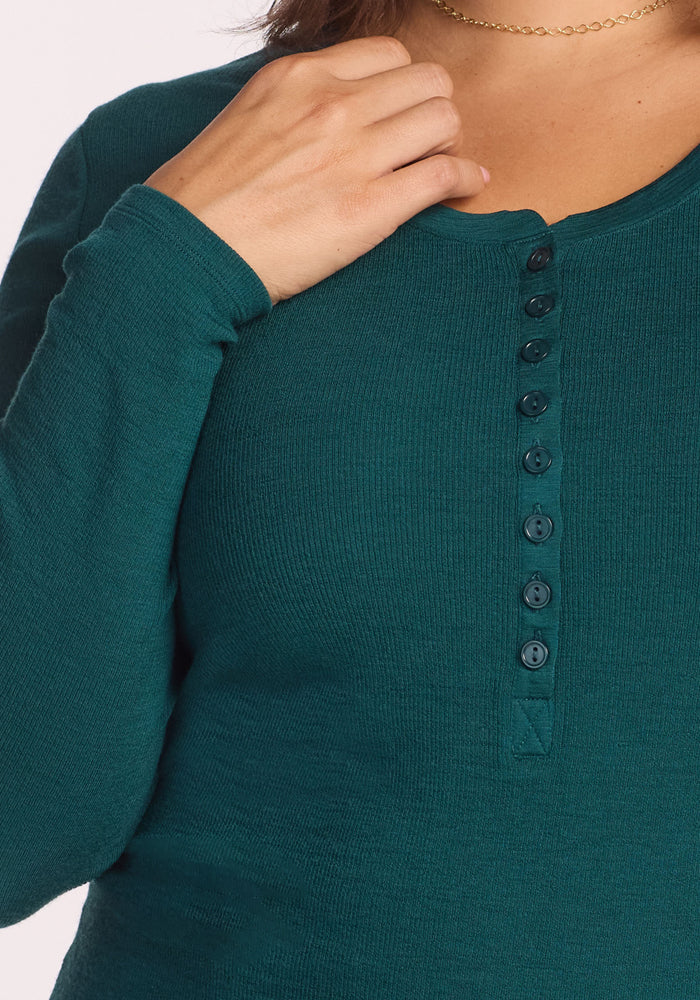 Close-up of a person wearing the Woolx Reese Ribbed Henley in Riverbank Green, featuring a partial button-up front and slim ribbed texture. They rest their hand on their collarbone, accessorized with a gold chain—ideal for winter layering.