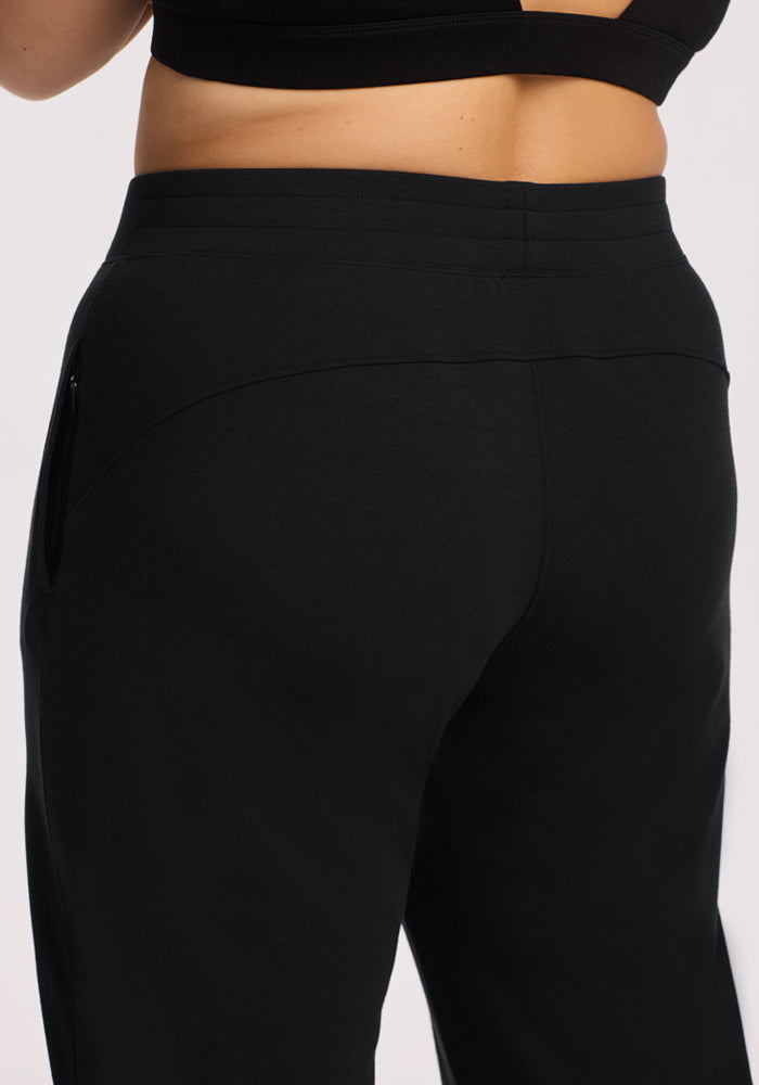 A close-up of a person wearing Woolx Brynn Pants - Black and a black sports bra, highlighting the waistband and upper back section of the pants.