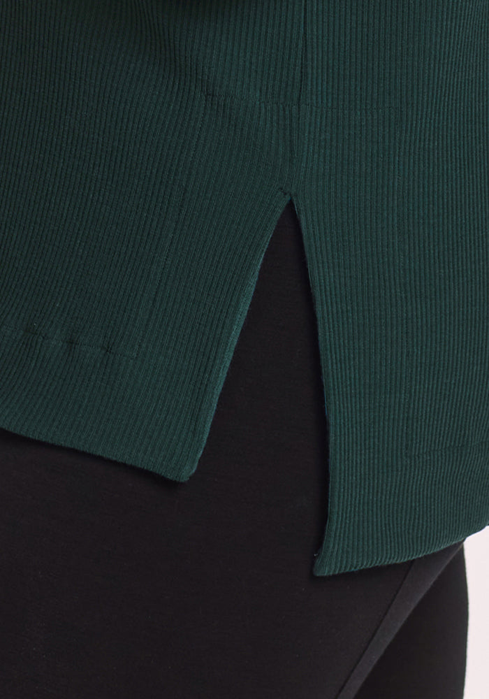 Close-up of the Woolx Ainsley Sweater in Deep Timber, featuring ribbed details and a side slit, styled over black pants.