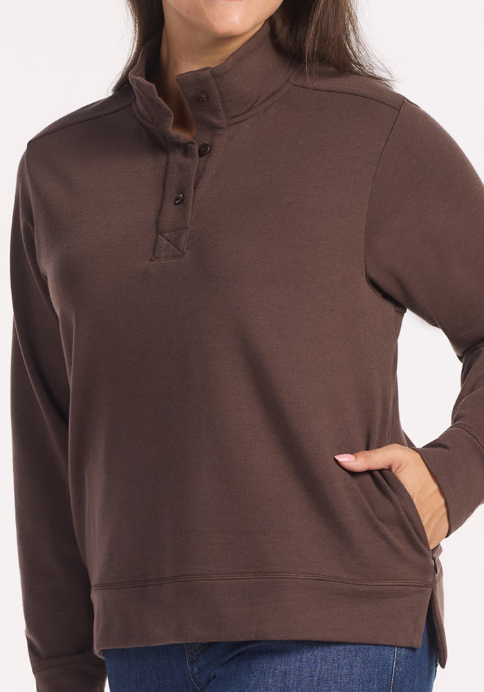 A person models the Woolx Annie 3 Button Pullover in Bracken, a brown heavyweight top with a button-up collar and side pocket—one hand in the pocket, the other relaxed—against a plain background.
