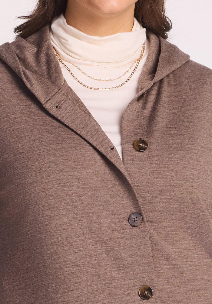 A person wears the Woolx Edna Hooded Cardigan in Simply Taupe over a cream turtleneck with layered gold chain necklaces. Only the lower face, neck, and upper torso are visible. Ideal for layering as a cold weather sweater.