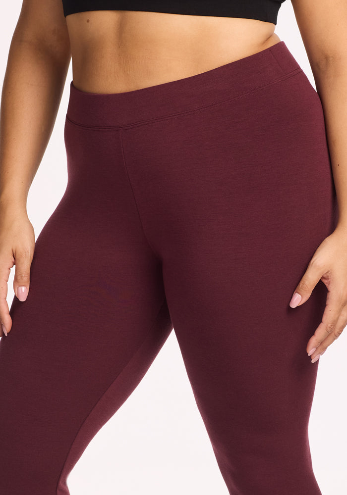 A person wearing Woolx Stella Leggings in Toasted Garnet, shown from mid-torso to mid-thigh, paired with a black cropped top and standing with one arm relaxed by their side.