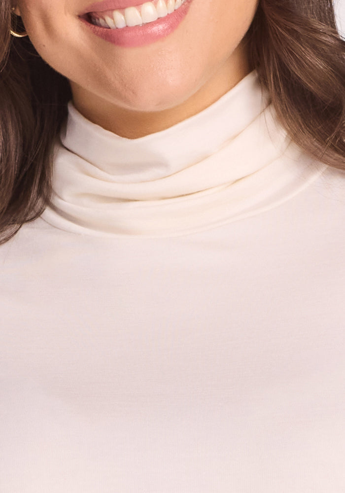Close-up of a woman smiling, showing part of her mouth and chin. She has long brown hair and is wearing the Woolx Kennedy Bodysuit in Buttercream, an essential layering piece for any wardrobe.