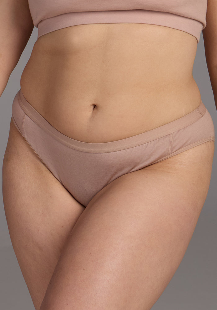 A person wears Woolx Roxie Bikini Underwear in Morning Latte—Merino wool, chafe-free bikini style—shown from shoulders to upper thighs against a neutral background.